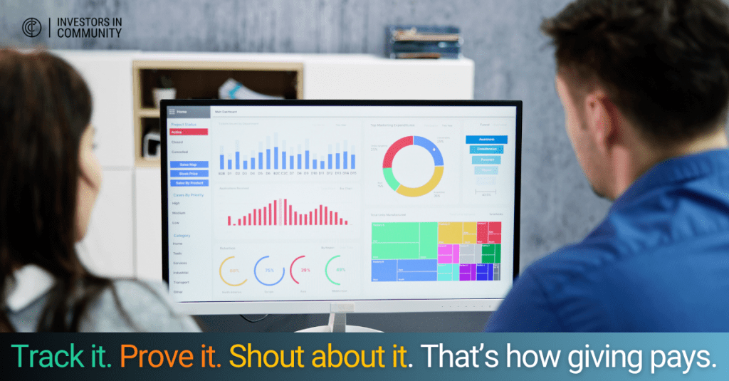 Two people with their backs to the camera looking at a computer screen displaying a digital dashboard with colourful charts and graphs. Along the bottom is a black and blue gradient banner with the words "Track it. Prove it. Shout about it. That's how giving pays.